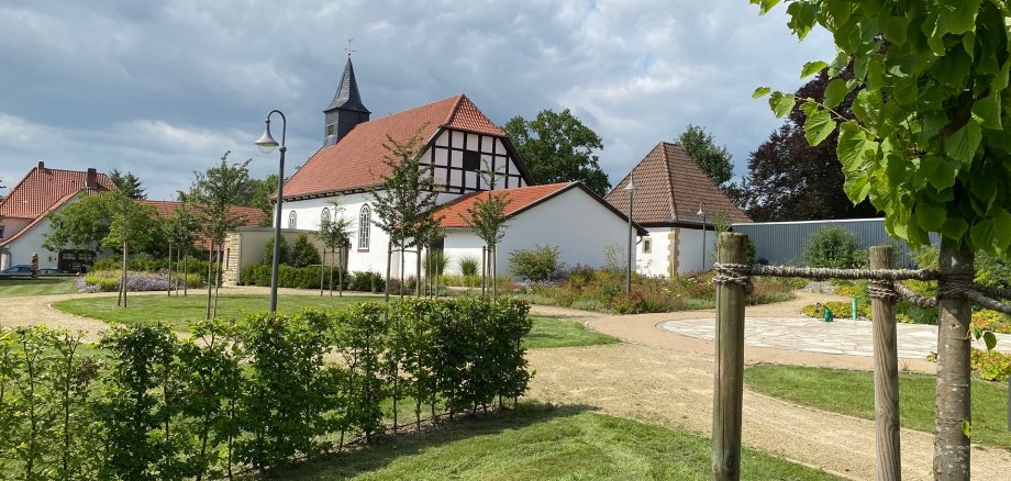 Ein bepflanzter Dorfplatz mit einer historischen Kapelle im Hintergrund.