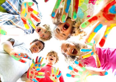 Mehrere Kinder mit bunt bemalten Shirts und Händen die im Kreis stehen und von oben hinab in die Kamera lachen. 