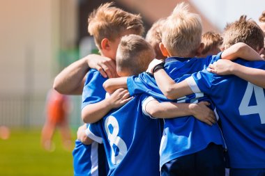 Spieler einer Kinderfußballmannschaft in blauen Trikots liegen sich in den Armen und freuen sich.