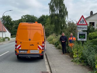 Ein in orange gekleideter Mitarbeiter des gemeindlichen Bauhofes montiert eine Geschwindigkeitsmesstafel an einem Straßenschild. 