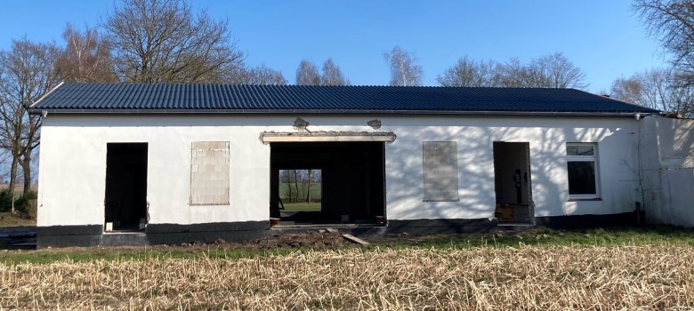 Ein Gebäude, ohne Fenster und Türen, das gerade umgebaut wird und sich noch im Rohbau befindet. Das Dach ist schon fertig. 