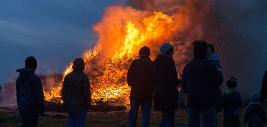 Mehrere Personen, die vor einem Brauchtumsfeuer stehen. 