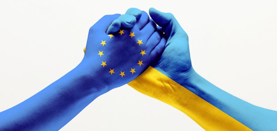 eine in den europäischen Farben bemalte Hand hält eine Hand, die in den ukrainischen Nationalfarben bemalt ist. 