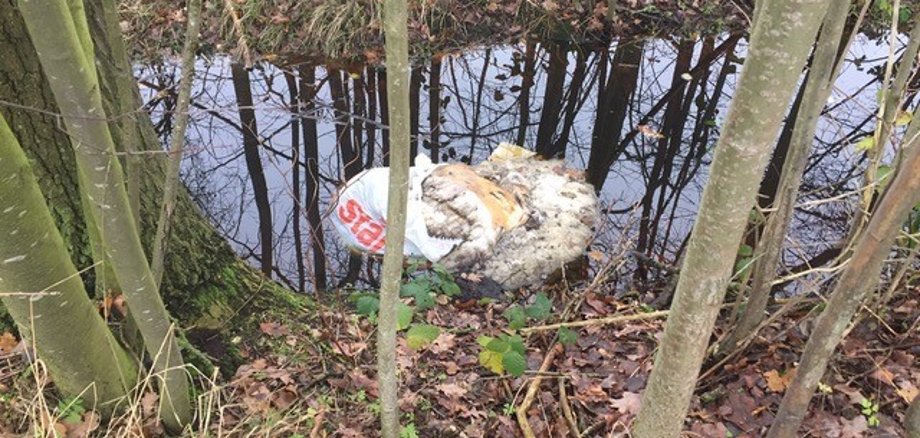 Ein gerissener Sack mit Schaffellen, der in einem Wassergraben liegt.