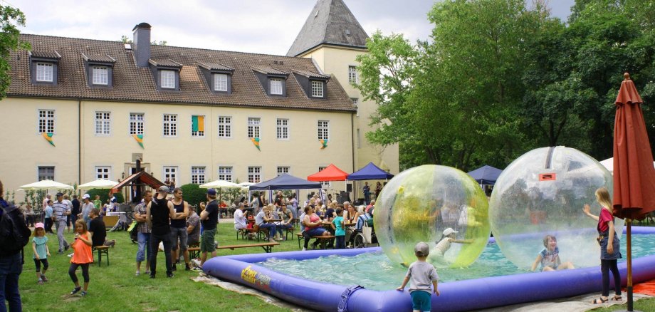 Reges Treiben anlässlich eines Sommerfestes im Garten des Haldemer Schlosses. Im Hintergrund ist ein gelbes Gebäude zu erkennen. 