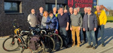 Eine Gruppe Radfahrerinnen und Radfahrer posiert für ein Gruppenfoto vor einem Feuerwehrgerätehaus.