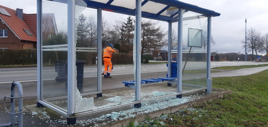 Ein zerstörtes, gläsernes Buswartehäuschen an einer Straße. Überall liegen Scherben.