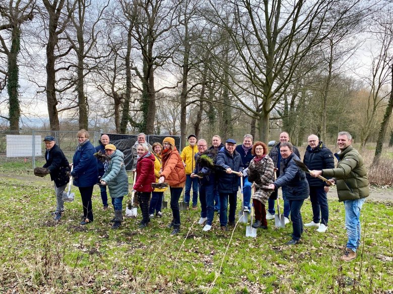 Eine Gruppe von rund 15 Erwachsenen, die in einem Park stehen und einen Spaten halten, als symbolisches Zeichen für den Baustart.  