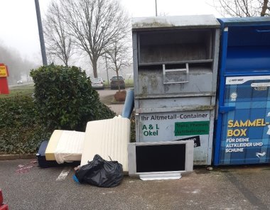 Ein Altkleidercontainer, vor dem unter anderem ein Fernseher und eine Matratze sowie ein gefüllter Müllsack abgeladen wurden.