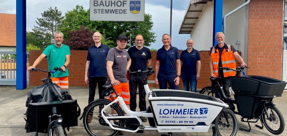 Sieben Männer, zum Teil mit oranger Arbeitskleidung stehen um drei Lasten-E-Bikes und schauen in die Kamera. Im Hintergrund ist das Schild "Bauhof Stemwede" zu erkennen.