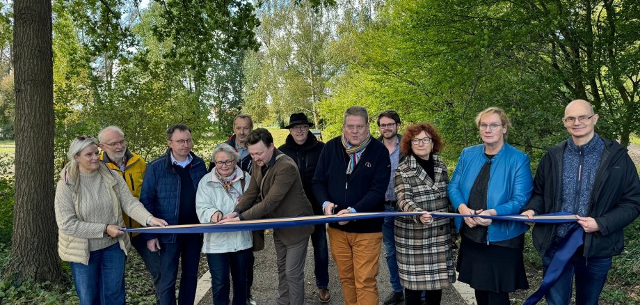 Bürgermeister Kai Abruszat und elf weiterer Personen schneiden symbolisch ein Band durch, um den Kurpark zu eröffnen.