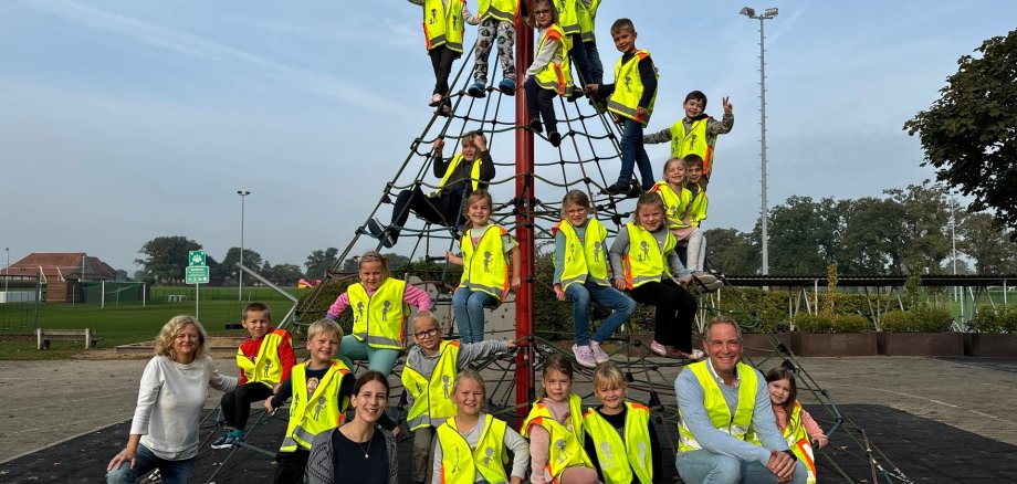 Die Erstklässlerinnen und Erstklässler der Grundschule Oppenwehe haben sich auf einem Klettergerüst verteilt. Sie alle trage die gelben Warnwesten. Auf dem Bild sind auch zwei Klassenlehrerinnen und ein Mitarbeiter der Gemeinde Stemwede zu sehen. 