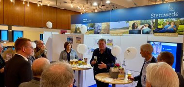 Ein Messestand, der laut der Beschriftungen an den Stellwänden zur Gemeinde Stemwede gehört. Zahlreiche Gäste informieren sich an dem Stand.