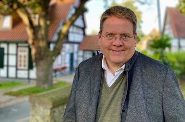 Ein Portraitfoto von Stemwedes Bürgermeister Kai Abruszat, auf dem im Hintergrund das historische Amtshaus in Levern zu erkennen ist.