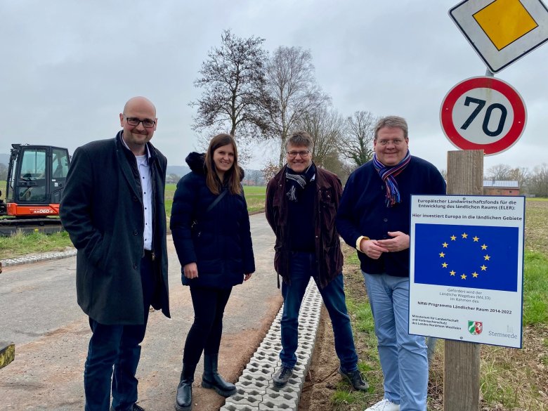 Gruppenfoto auf der Baustelle. Eine Frau und drei Männer stehen an einem Schild, dass auf die Fördermaßnahme hinweist, durch das die Bauarbeiten ermöglicht werden.