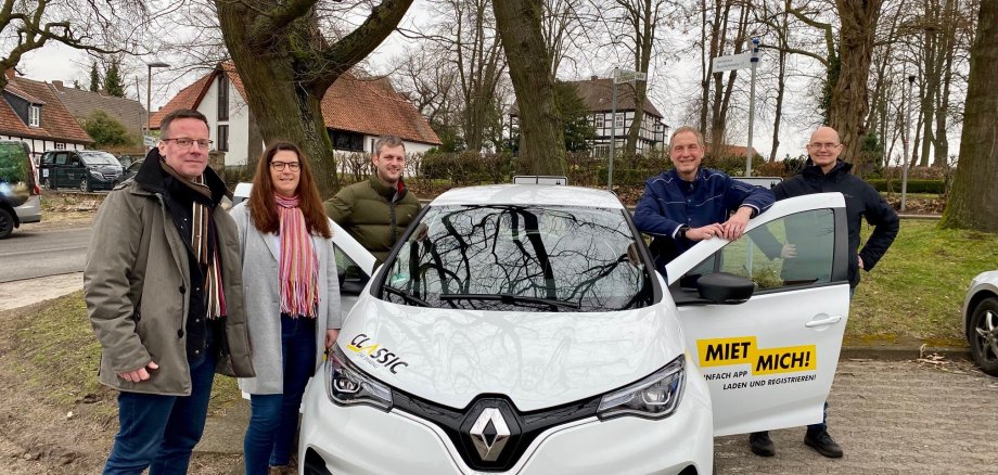 Gruppenfoto mit fünf Erwachsenen, die um ein weißes Auto stehen.