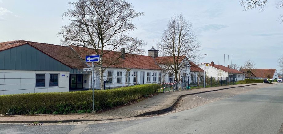 Ein weißes Schulgebäude mit einer davor verlaufenden Bushaltestelle an einer Straße. 